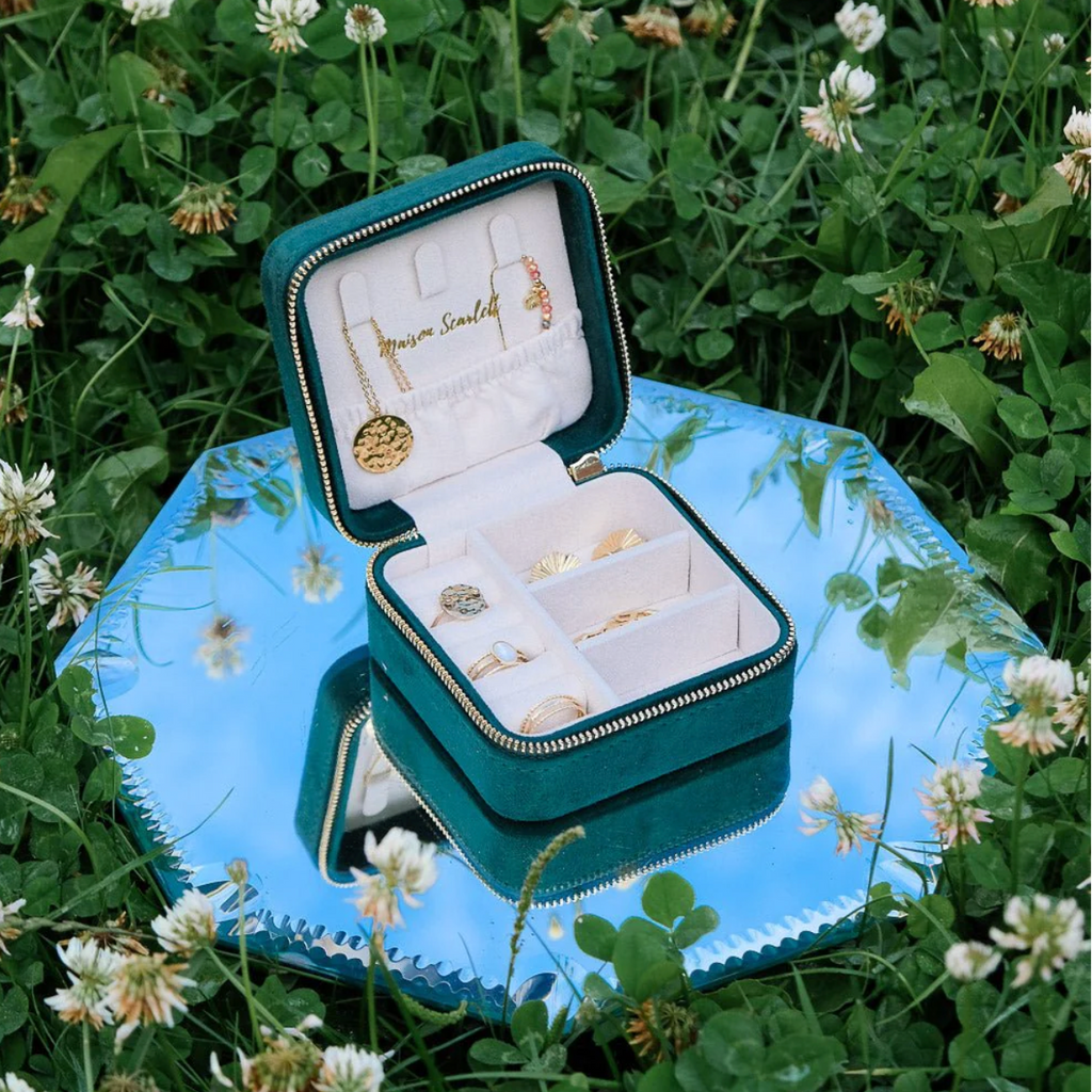 Open groene velours reissieradendoos van Maison Scarlett met sieraden op een blauw dienblad in het gras