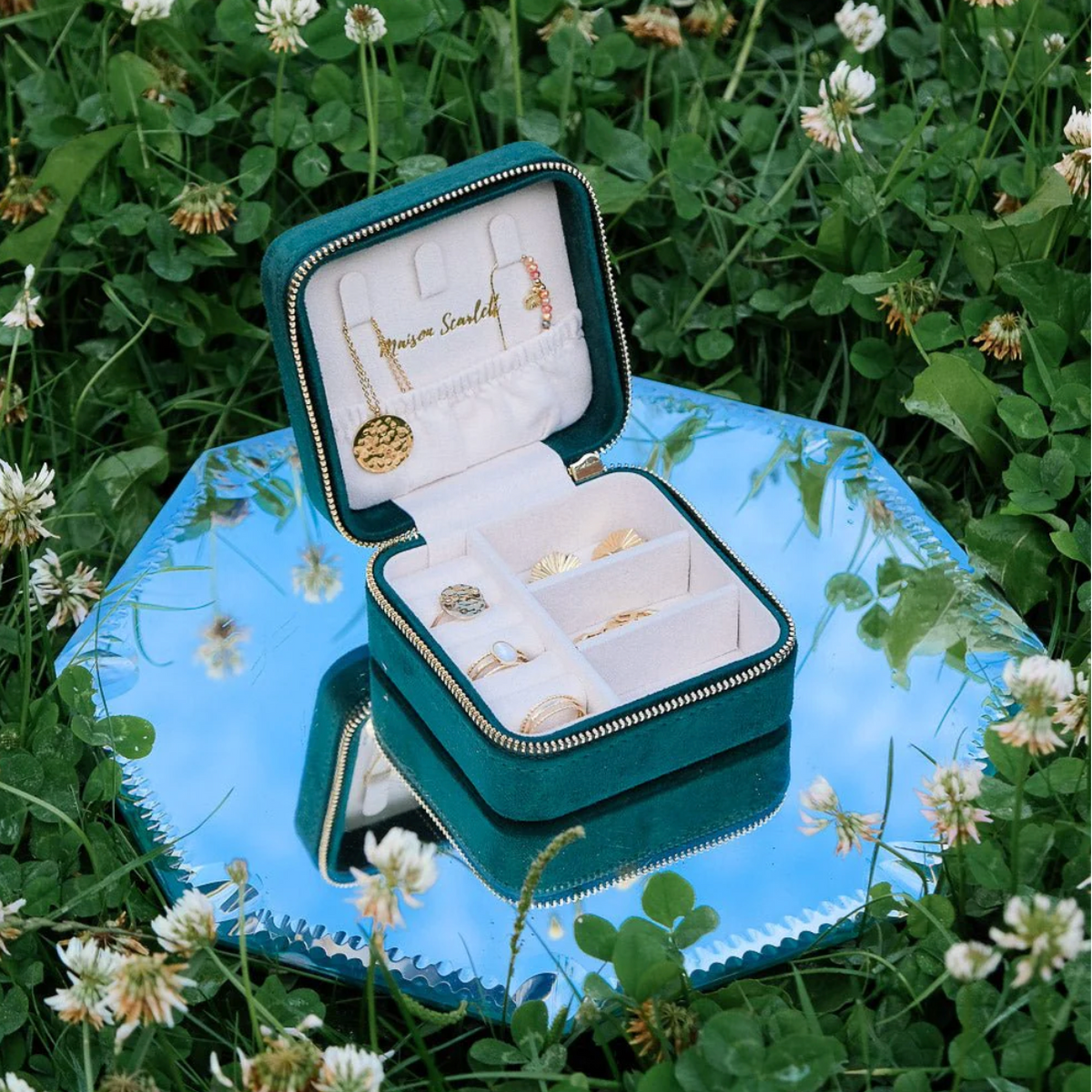 Open groene velours reissieradendoos van Maison Scarlett met sieraden op een blauw dienblad in het gras
